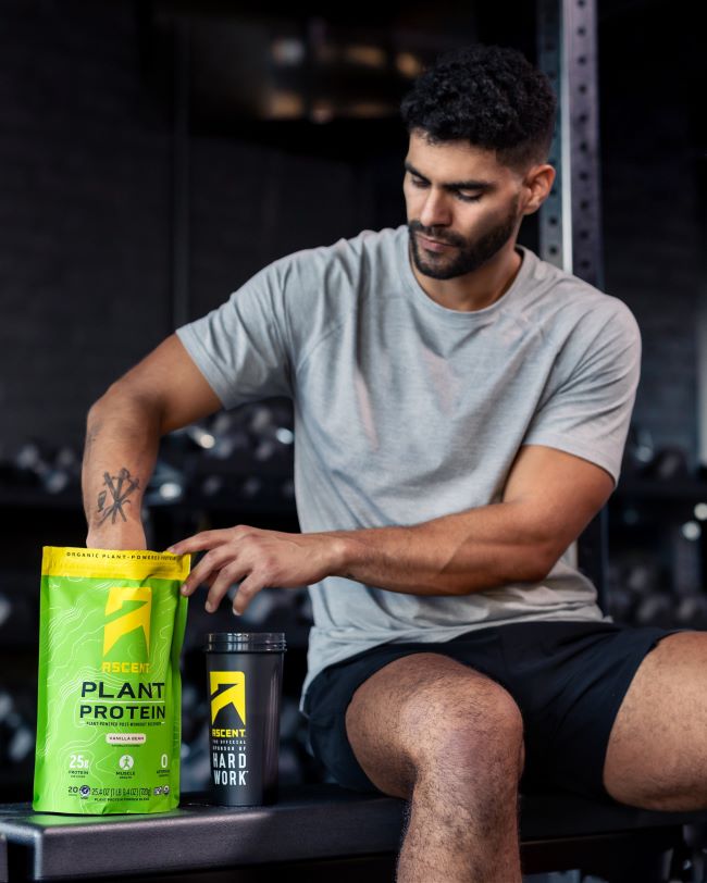 ascent protein athlete scoping vanilla vegan protein powder from the bag into a protein powder blender while at the gym