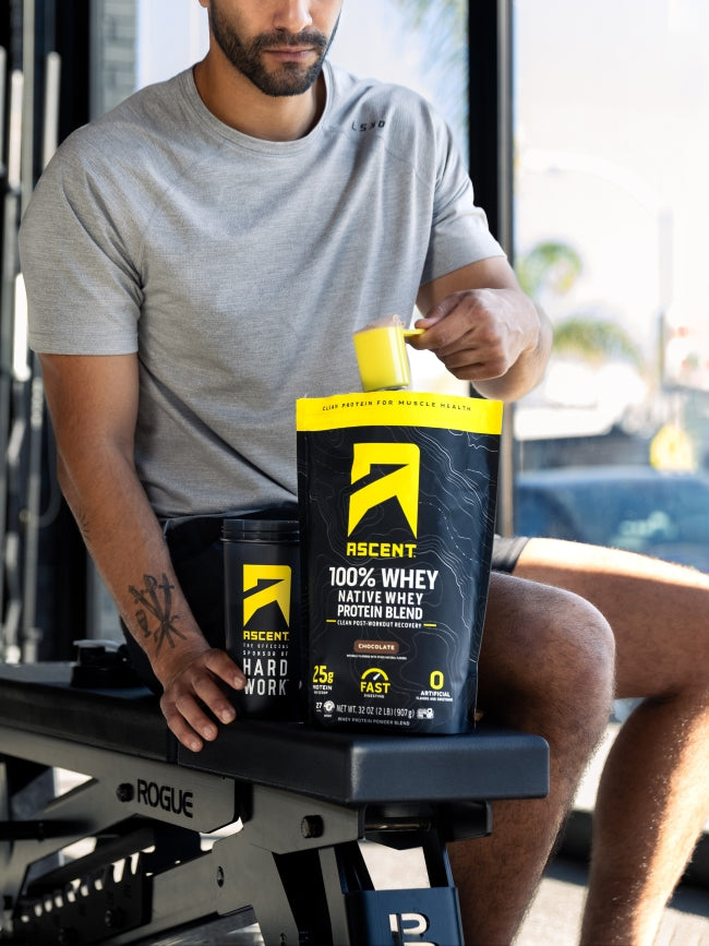 ascent protein athlete scooping protein powder into a blender bottle at the gym