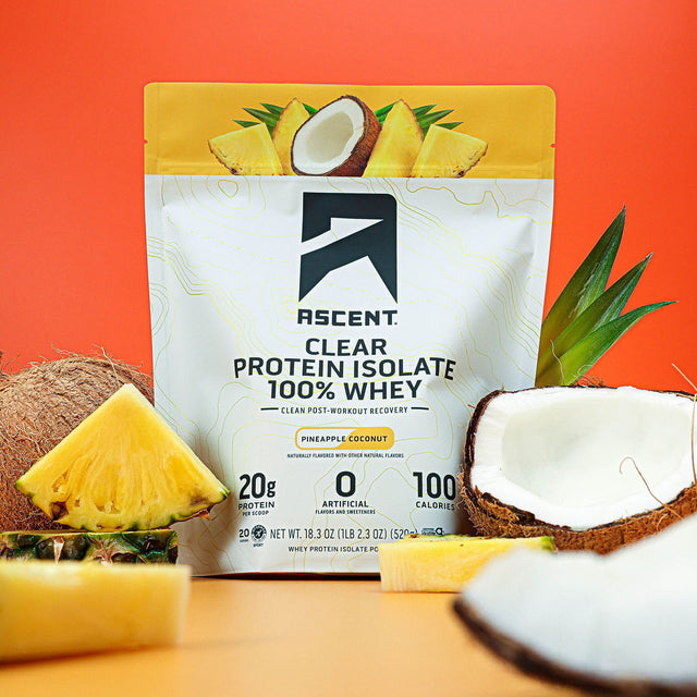 A bag of Pineapple Coconut Clear Whey sitting next to slices of pineapple and coconuts that have been cracked open.