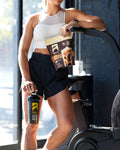 female athlete in a gym holding a bag of protein powder and cup