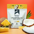 A bag of Pineapple Coconut Clear Whey sitting next to slices of pineapple and coconuts that have been cracked open.