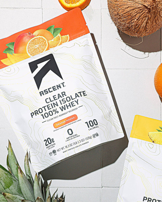 Rescent Clear Isolate protein powder package on a white surface with fruits and a coconut.