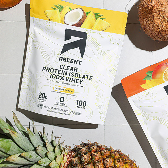 Ascent Clear Protein Isolate 100% Whey package on a table with a coconut and pineapple.