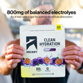 A person holds up a packet of Ascent Clean Hydration Electrolyte Drink Mix in Passion Fruit flavor. The packet is white with purple passion fruit graphics and black text.
