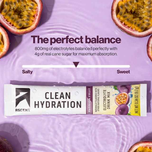 A tube of ASCENT Clean Hydration electrolyte drink mix in passion fruit flavor, placed on a purple liquid surface with ripened passion fruit slices around the edges. Text above reads 'The perfect balance' with a salty-to-sweet balance slider.