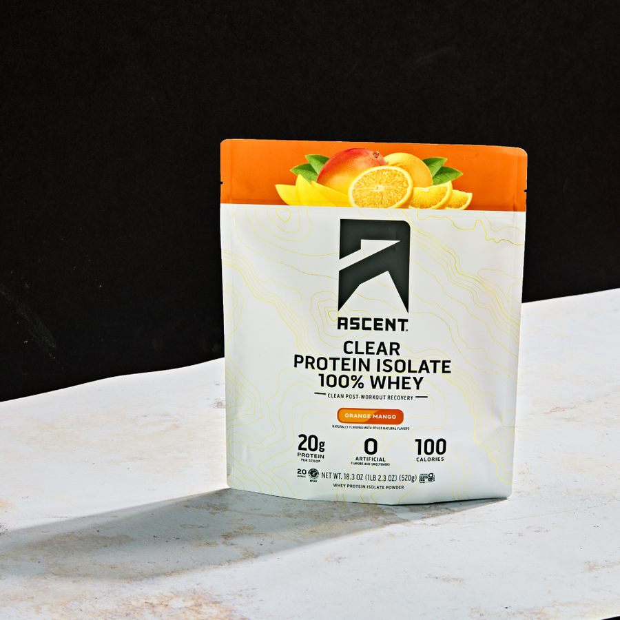 A sealed pouch of Ascent Clear Whey Protein Isolate with an orange and mango flavor theme, displaying 20g of protein per serving and no artificial flavors or sweeteners.