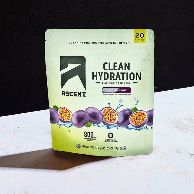 A stand-up pouch of Ascent Clean Hydration electrolyte drink mix in passionfruit flavor, standing on a white surface against a black background.