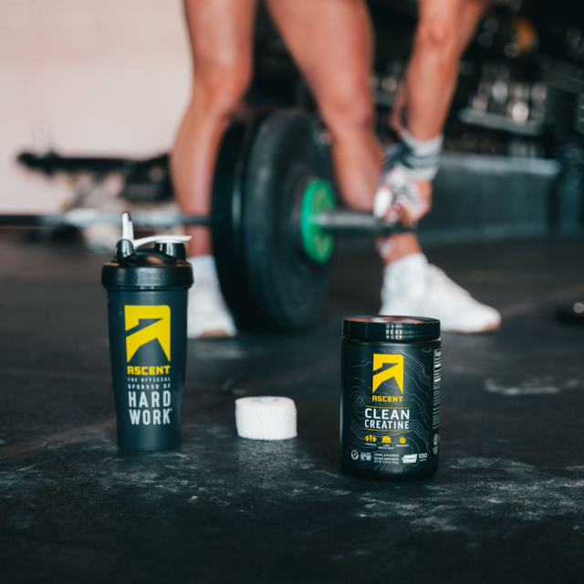 Pre-workout supplement containers on a gym floor with a person lifting weights.