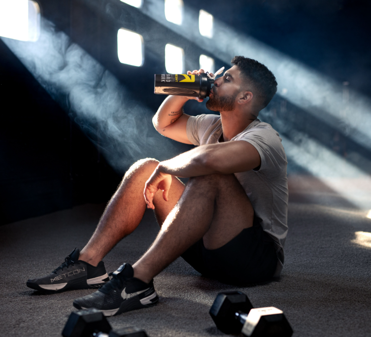A man sitting on the ground and drinking from an Ascent shaker bottle.