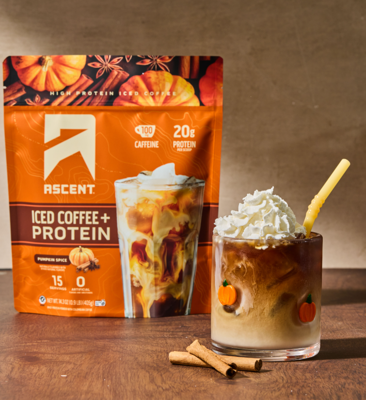 a bag of pumpkin spice iced coffee + protein from Ascent next to a latte with whipped cream and cinnamon sticks