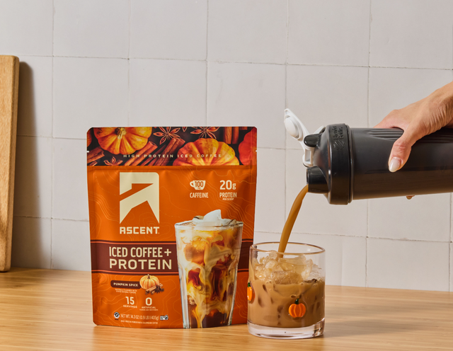 a bag of pumpkin spice iced coffee + protein from Ascent next to a glass being filled with pumpkin spice iced coffee + protein from a shaker bottle