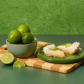Lime slices and a bowl of limes on a wooden cutting board with a green background