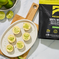 Key lime pies on a plate with a package of Ascent protein powder on a marble surface.