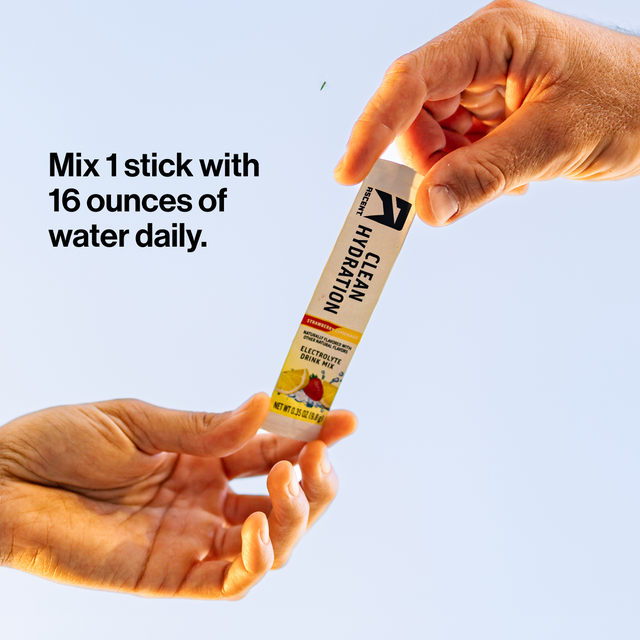 Two hands holding a single stick of Clean Hydration electrolyte powder against a light blue background, with text reading 'Mix 1 stick with 16 ounces of water daily.'.