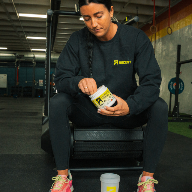 female athlete in a gym holding an open jar of clean hydration + energy powder