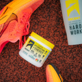 jar of clean hydration + energy powder on a track & field track with shoes and cup next to it