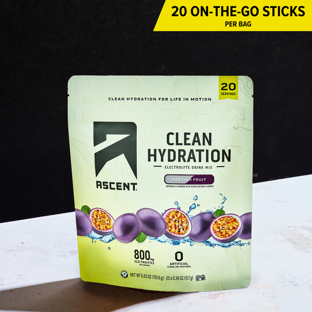 A stand-up pouch of Ascent Clean Hydration electrolyte drink mix in passion fruit flavor, shown on a white surface against a black background. A yellow banner at the top reads '20 ON-THE-GO-STICKS PER BAG'.