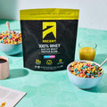 Ascent 100% Fruity Cereal Whey Protein Blend package on a table with bowls of cereal and drinks.