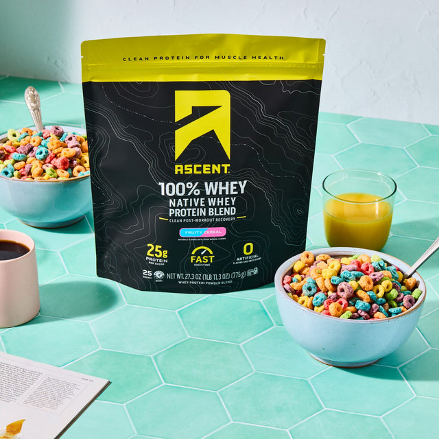 Ascent 100% Fruity Cereal Whey Protein Blend package on a table with bowls of cereal and drinks.