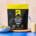 Ascent Fruity Cereal Whey Protein Blend package on a table with cereal and a glass of milk.