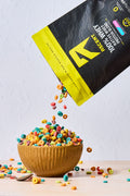 Bag of Ascent 100% Whey native whey protein blend being poured into a wooden bowl with colorful cereal pieces on a light background