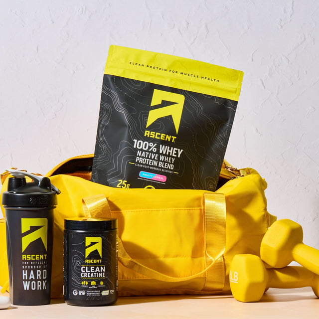 Ascent protein products including a bag, shaker, and creatine with dumbbells on a light background