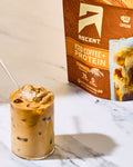 Glass of iced coffee with protein next to a box of Ascent iced coffee and protein on a marble surface.