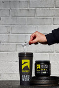 Person pouring 'Ascent Clean Creatine' powder into a large cup.