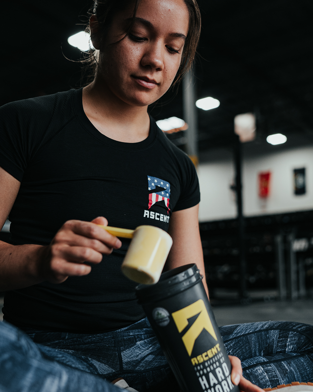 female athlete in a gym scooping protein powder into an Ascent cup